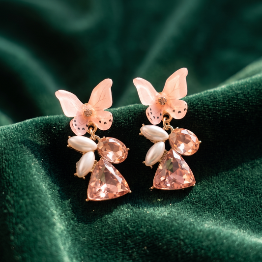 Butterfly-shaped earrings with pink and white stones on a green fabric background