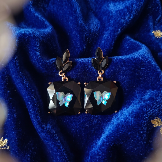 Pair of earrings with butterfly designs on a blue velvet background