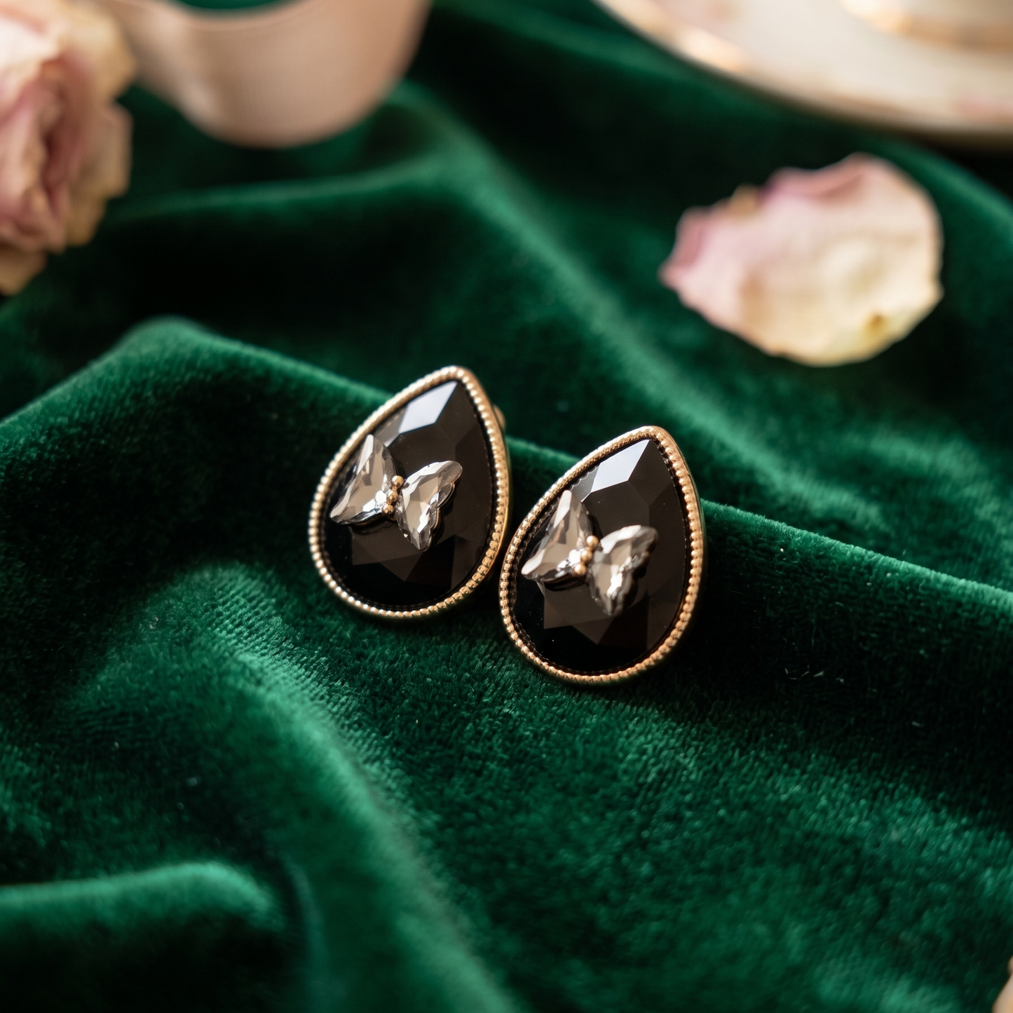 Black teardrop earrings with gold accents on a green fabric background