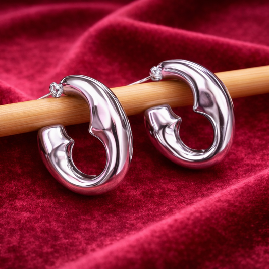 Silver hoop earrings on a wooden stick against a red fabric background