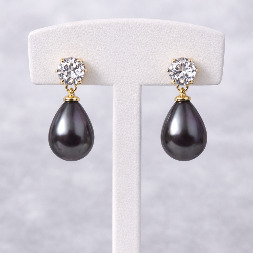 Pair of black teardrop earrings with gold and crystal accents on a white stand against a light gray background.