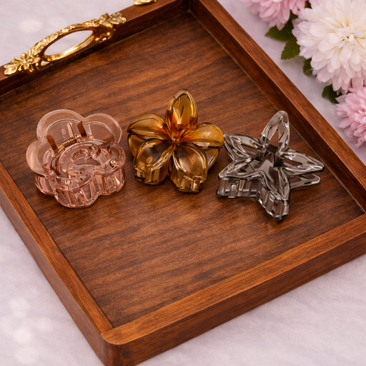 Three decorative hair clips on a wooden tray with flowers in the background