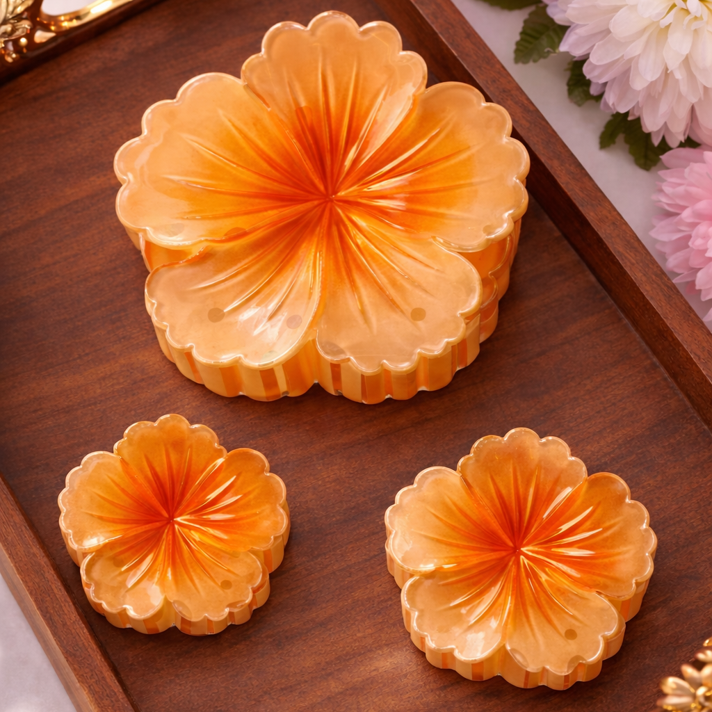 Three orange flower-shaped pastries on a wooden tray with floral decorations in the background.
