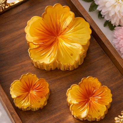 Three yellow floral pastries on a wooden tray with decorative handles, surrounded by flowers.