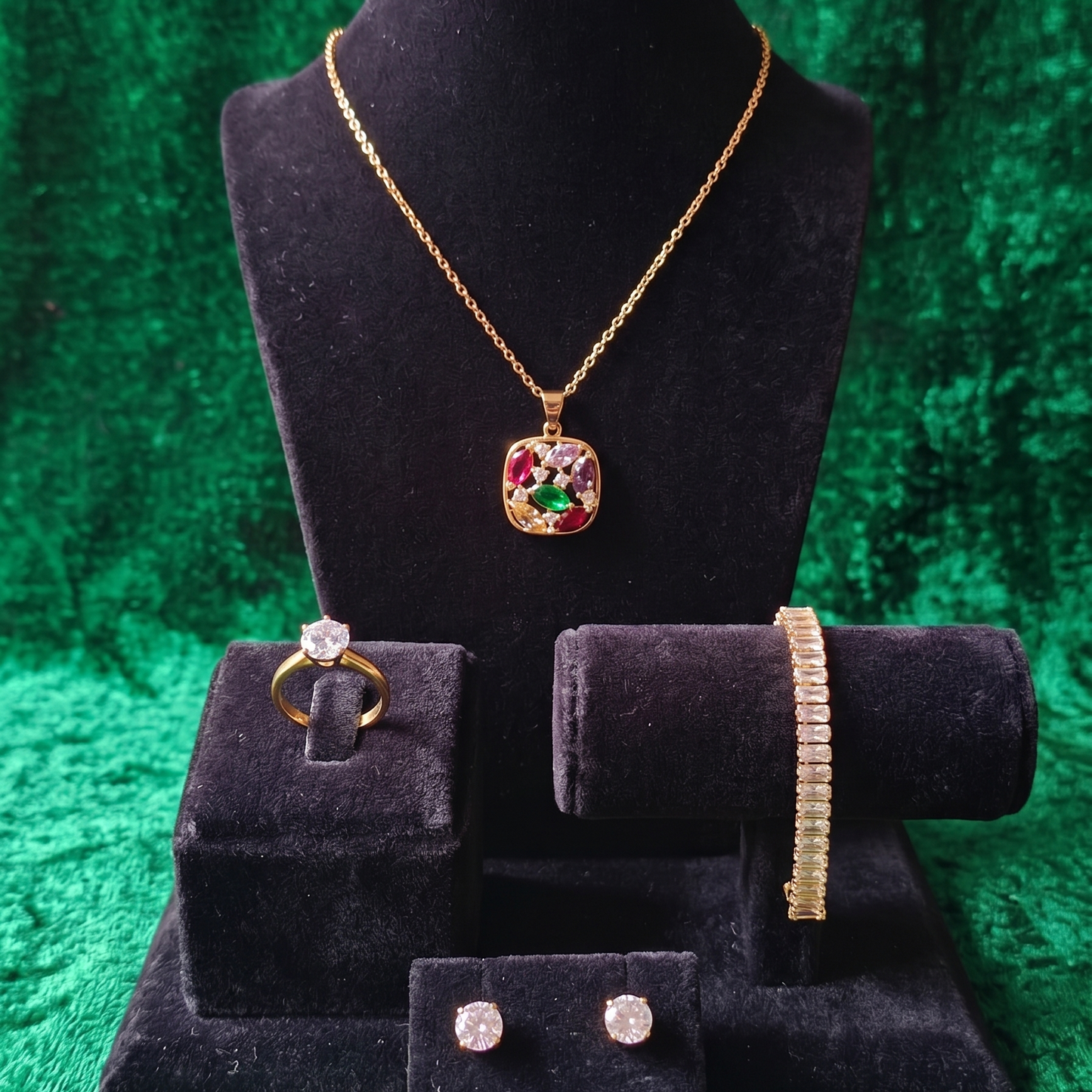 Jewelry set including a necklace, ring, bracelet, and earrings on black velvet stands against a green textured background.