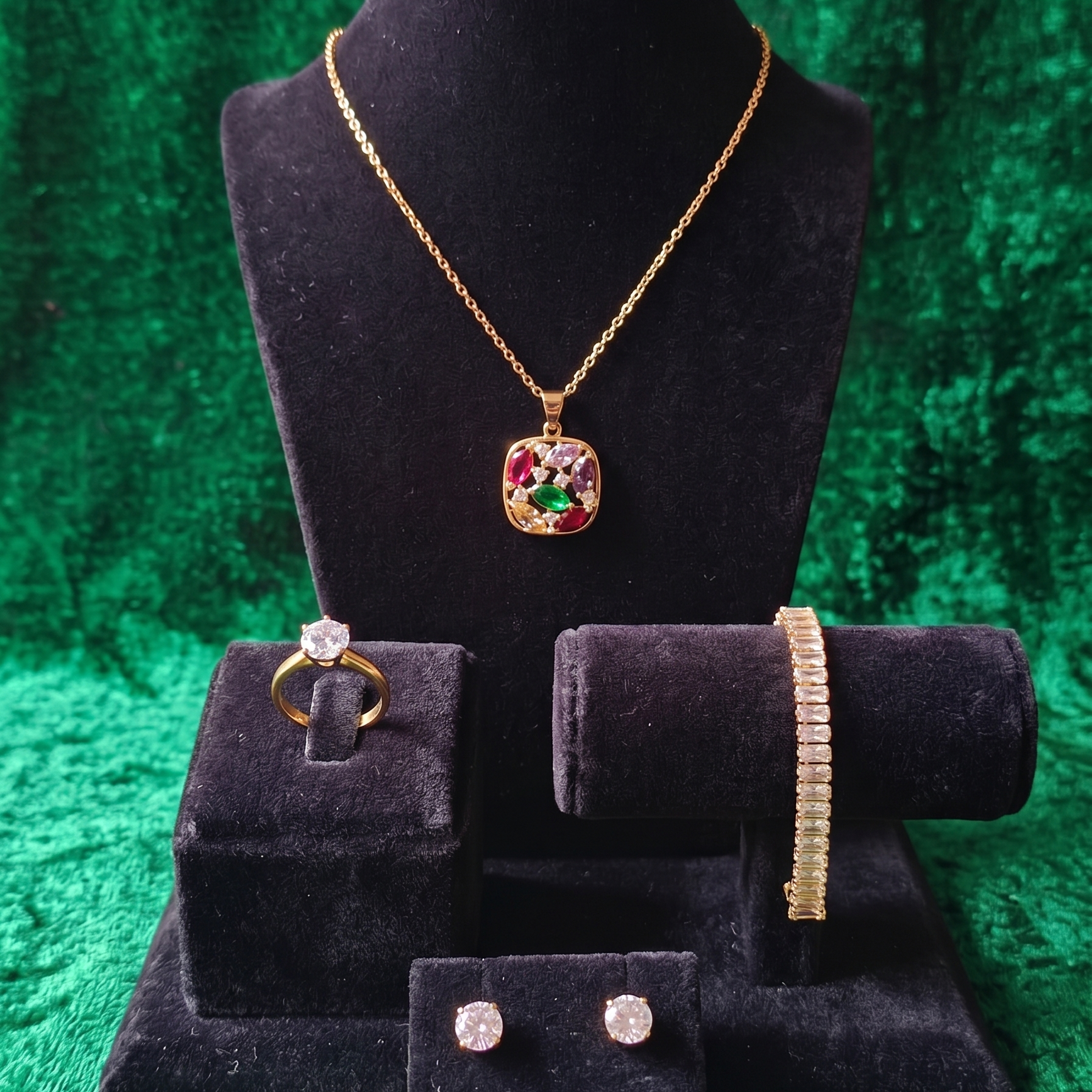 Jewelry set including a necklace, ring, bracelet, and earrings on black velvet stands against a green textured background.