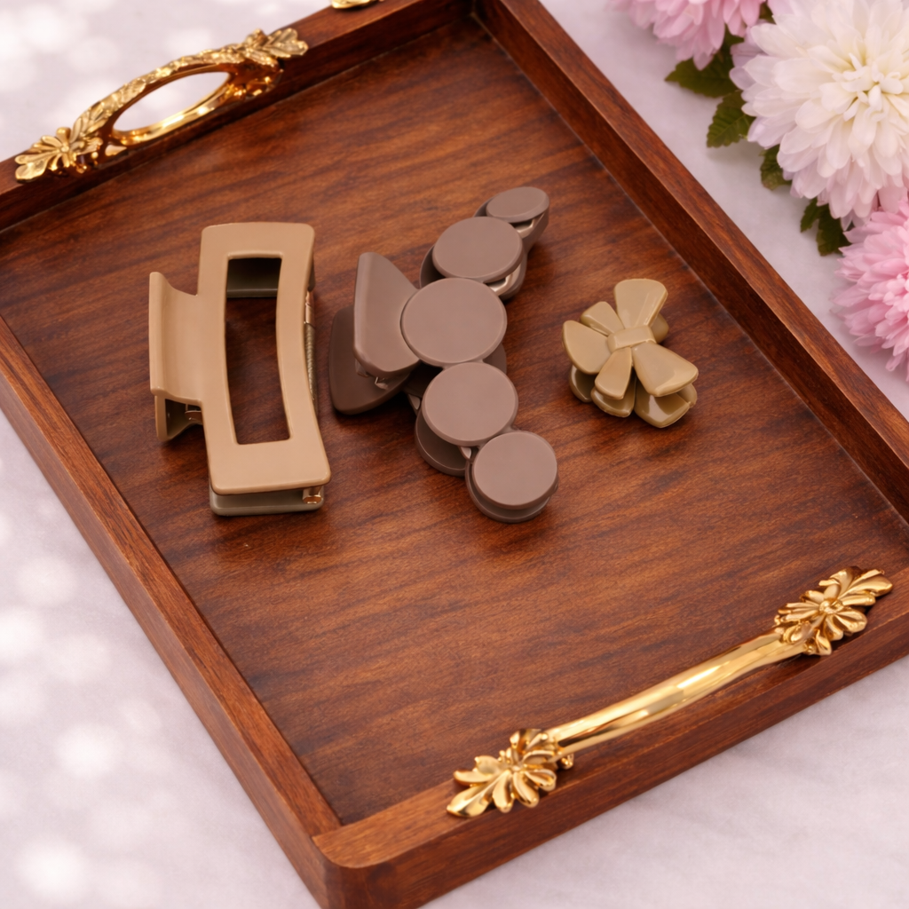 Decorative wooden tray with gold and bronze hair clips on a white surface with flowers.