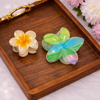 Two colorful flower-shaped hair clips on a wooden tray with flowers in the background.