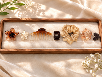 Set of hair accessories including a comb, flowers, and scrunchies on a wooden tray with a soft background.