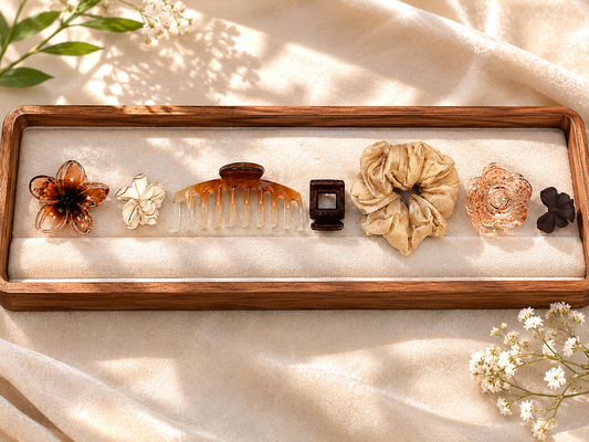 Set of hair accessories including a comb, flowers, and scrunchies on a wooden tray with a soft background.