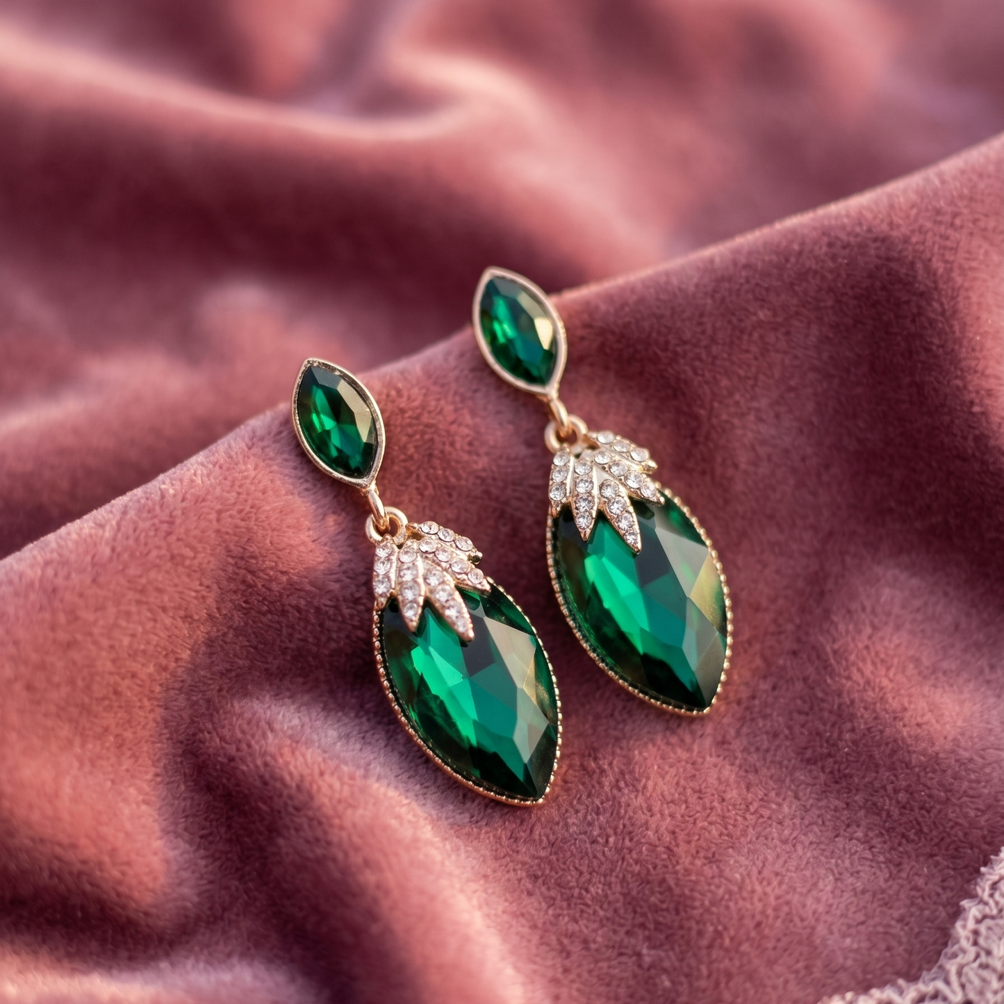 Green teardrop earrings with gold accents on a textured brown fabric background