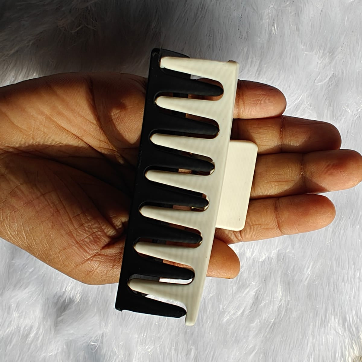 Hand holding a black and beige comb against a neutral background