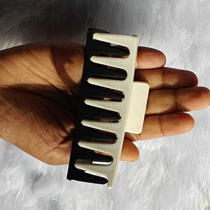 Hand holding a black and beige comb against a neutral background