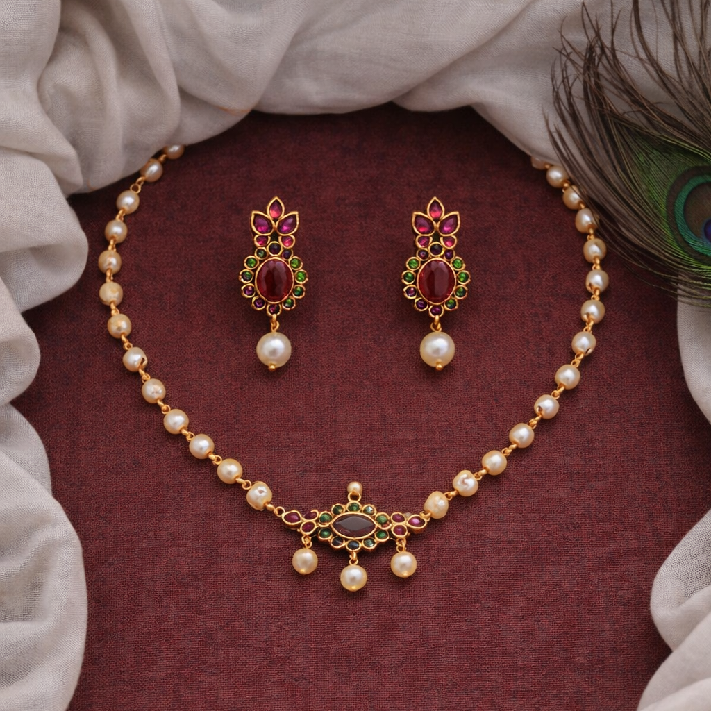 Pearl necklace and earrings set on a maroon fabric background with peacock feather