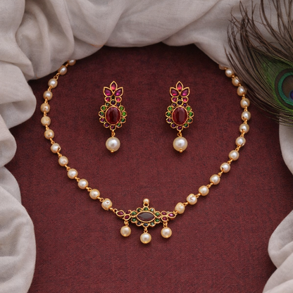 Pearl necklace and earrings set on a maroon fabric background with peacock feather