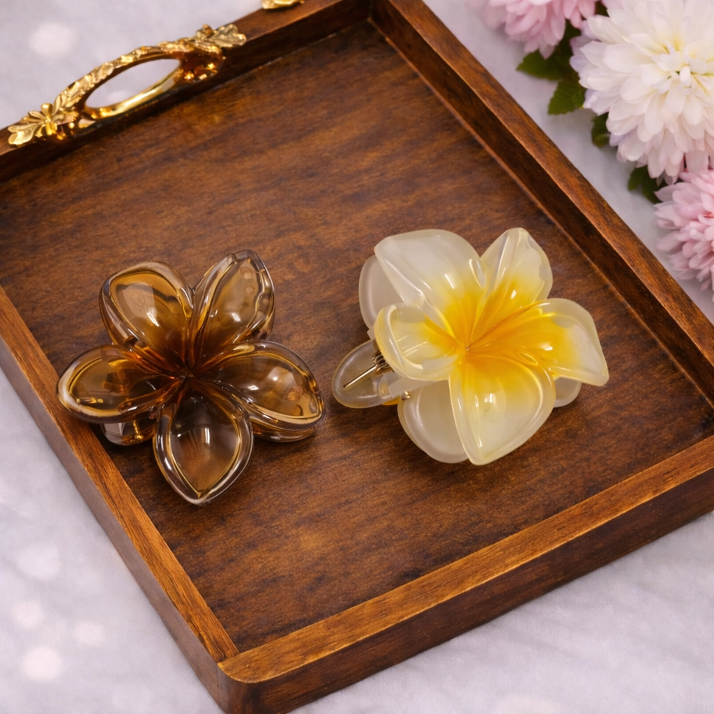 Two flower-shaped hair clips on a wooden tray with flowers in the background