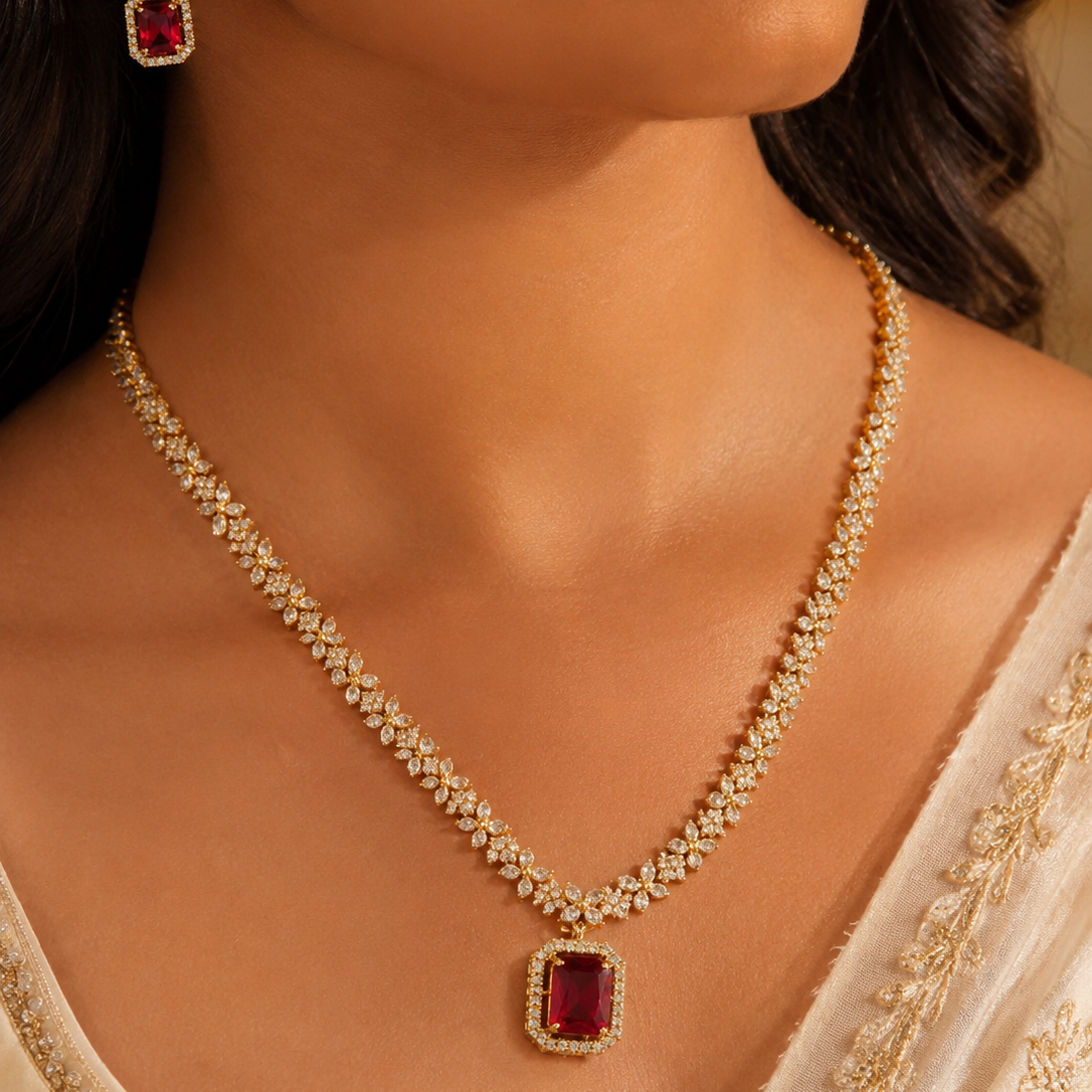 Close-up of a woman wearing a gold necklace with a red gemstone pendant and matching earrings.