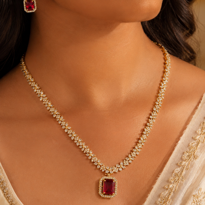 Close-up of a woman wearing a gold necklace with a red gemstone pendant and matching earrings.