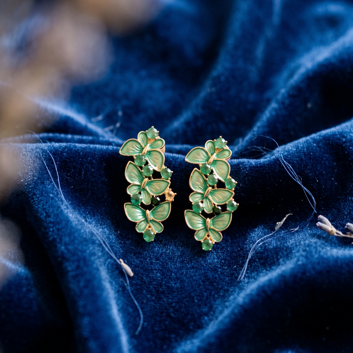 Green leaf-shaped earrings on a blue fabric background