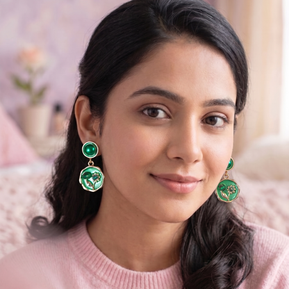 Woman wearing green earrings with a pink sweater in a softly blurred indoor setting