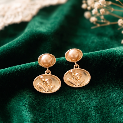 Gold earrings on a green fabric background with dried flowers.