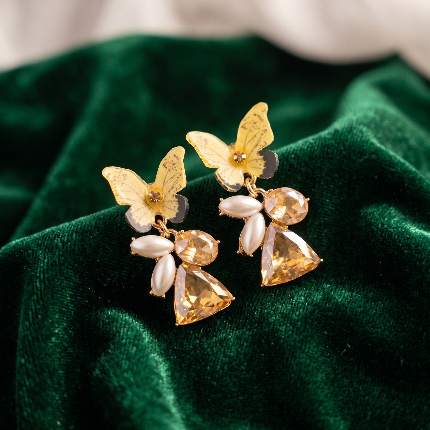 Butterfly-shaped earrings with gold and clear stones on a green velvet background
