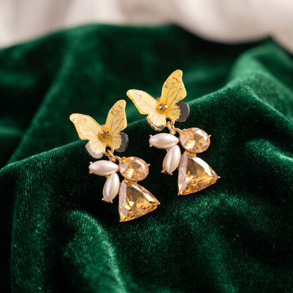 Butterfly-shaped earrings with gold and clear stones on a green velvet background