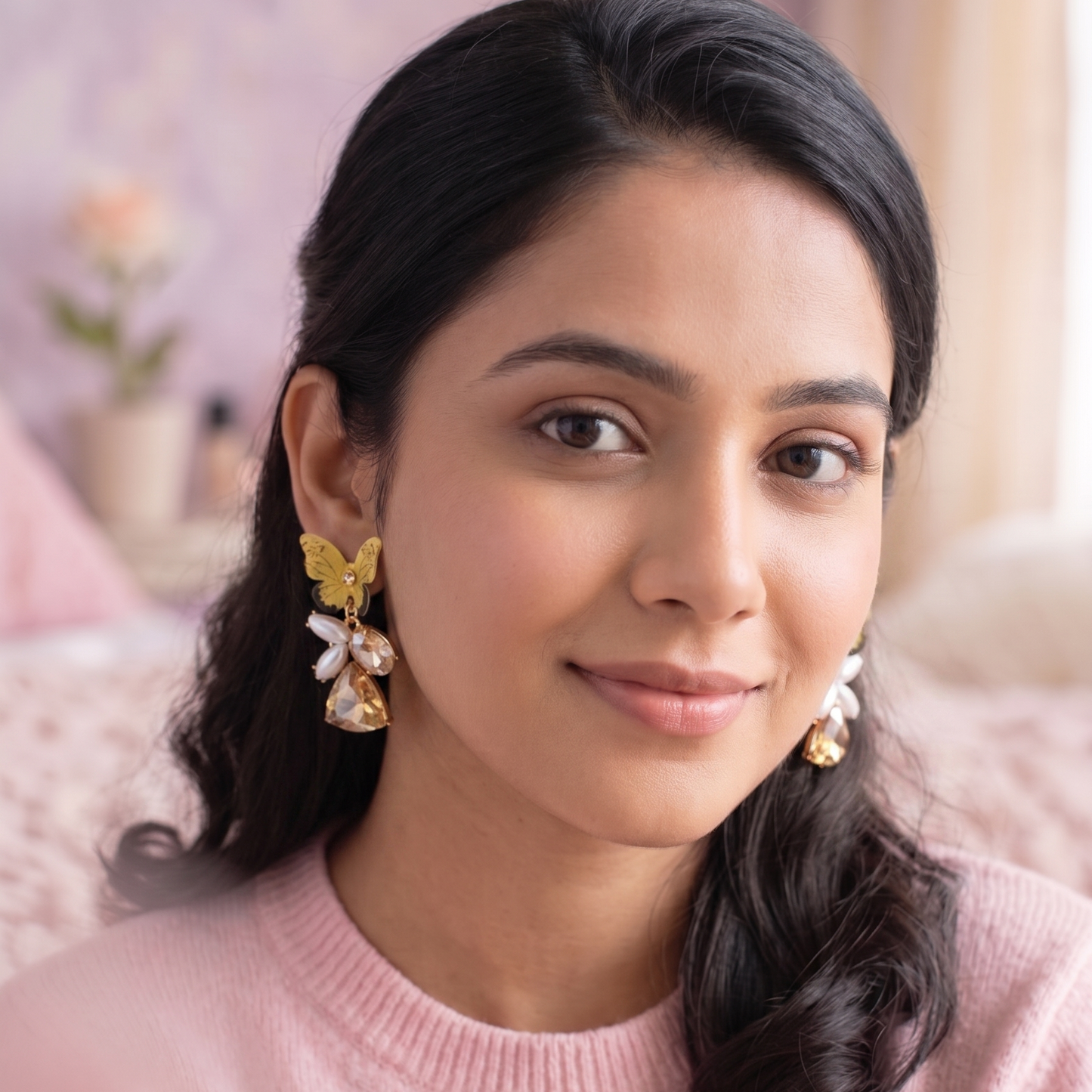 Woman wearing gold earrings with a pink sweater in a soft, blurred indoor setting