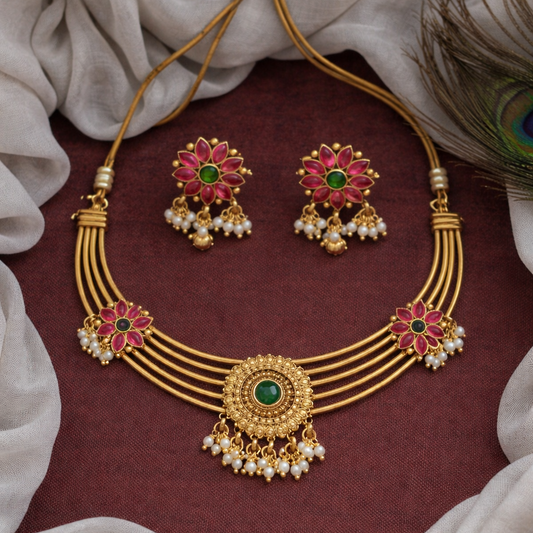 Gold necklace with pink and green gemstones on a maroon fabric background