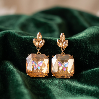Pair of gold earrings with butterfly designs on a green fabric background