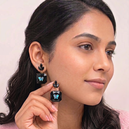 Woman wearing black earrings with blue gemstones, holding one earring close to her face.