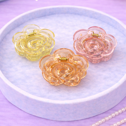 Three colorful flower-shaped hair clips on a white plate with a purple background.