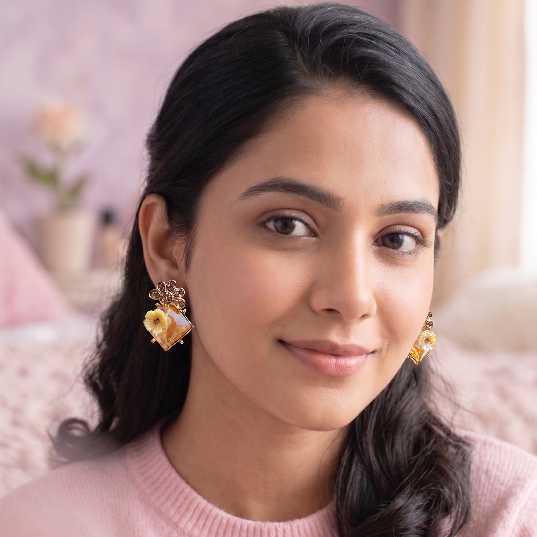 Woman wearing gold earrings with a pink sweater in a soft, blurred indoor setting