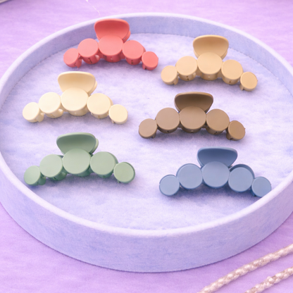 Set of colorful hair clips on a round white tray with a purple background