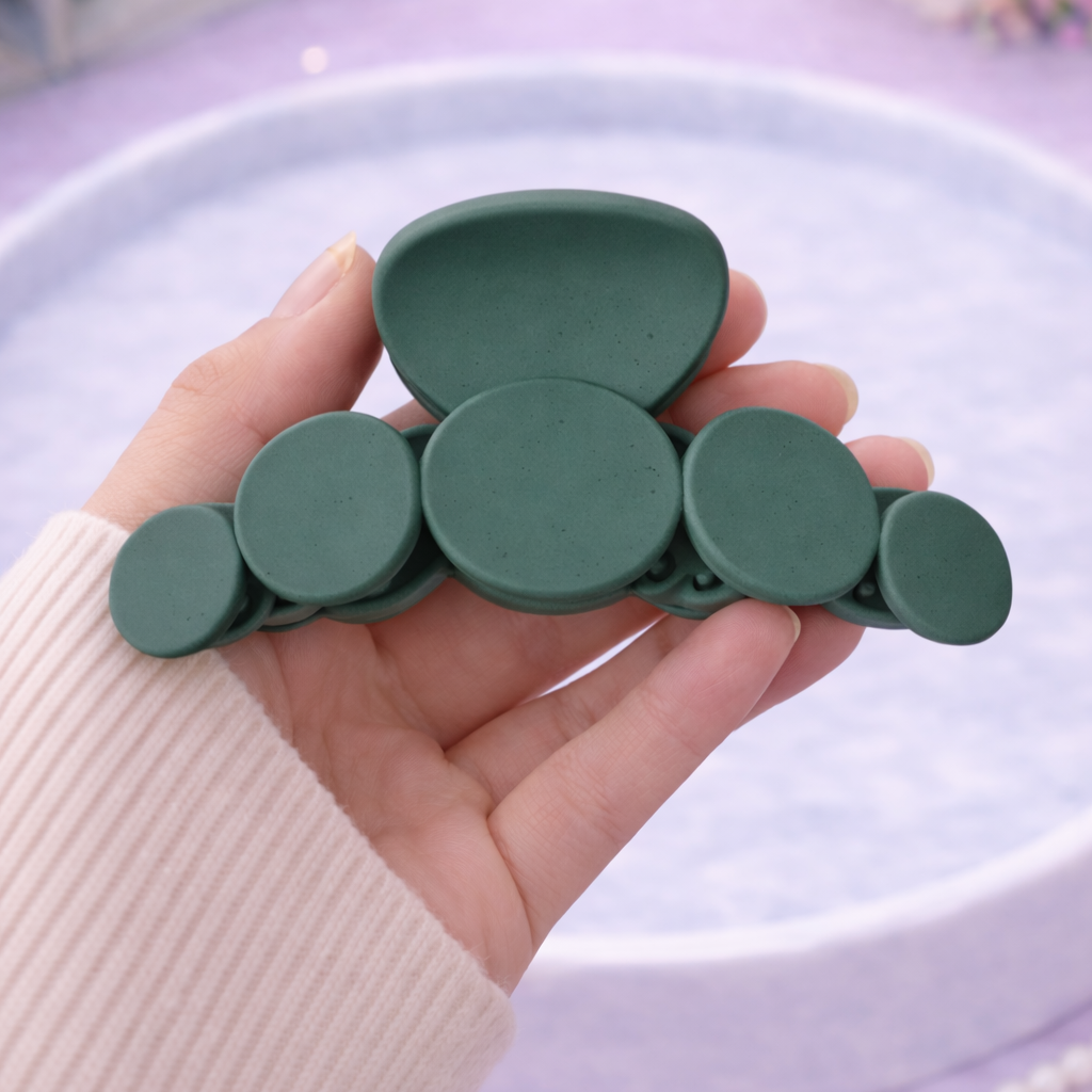 Green hair clip held by a hand on a light purple surface with flowers in the background