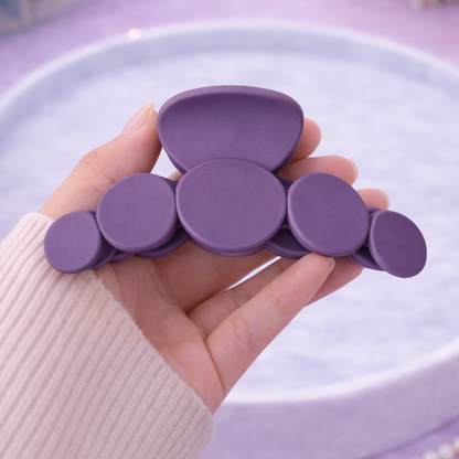 Hand holding a purple hair clip against a light purple background