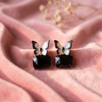 Butterfly-shaped earrings with black gemstones on a pink fabric background