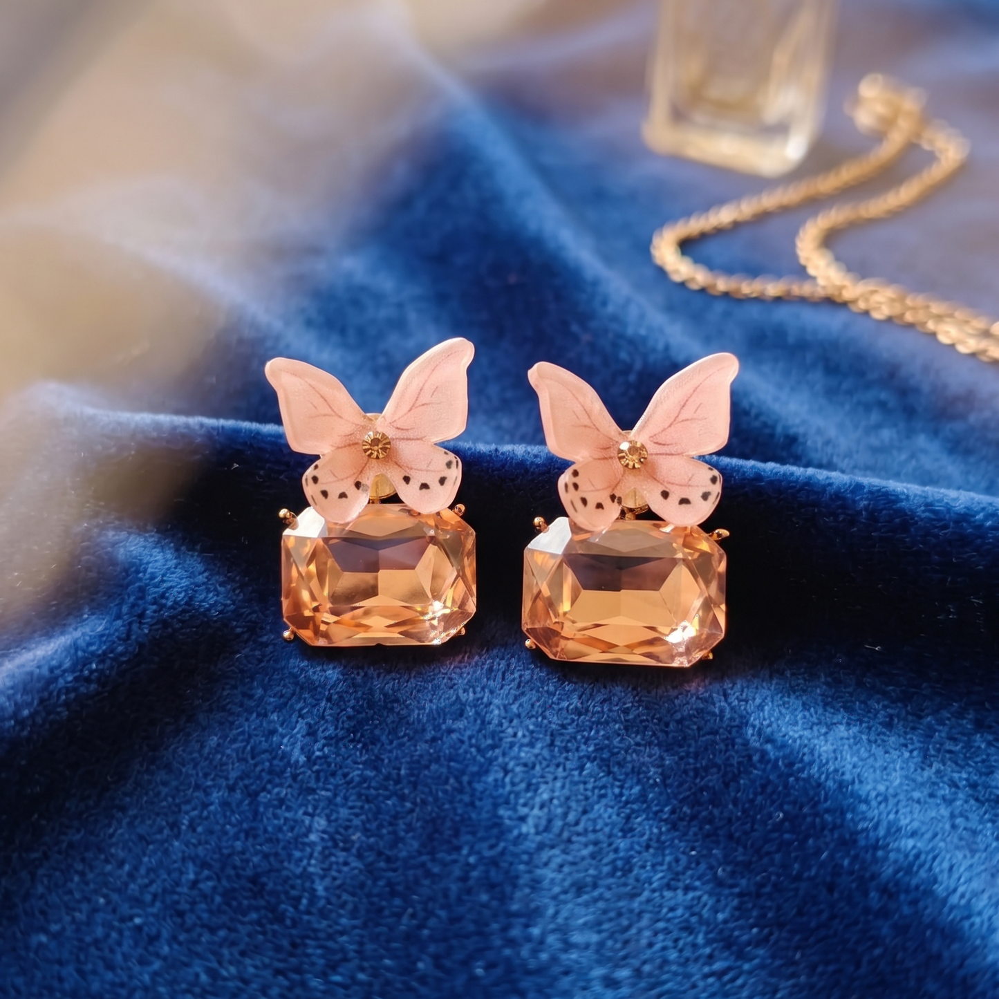 Butterfly-shaped earrings on a blue fabric background with a bottle of perfume.