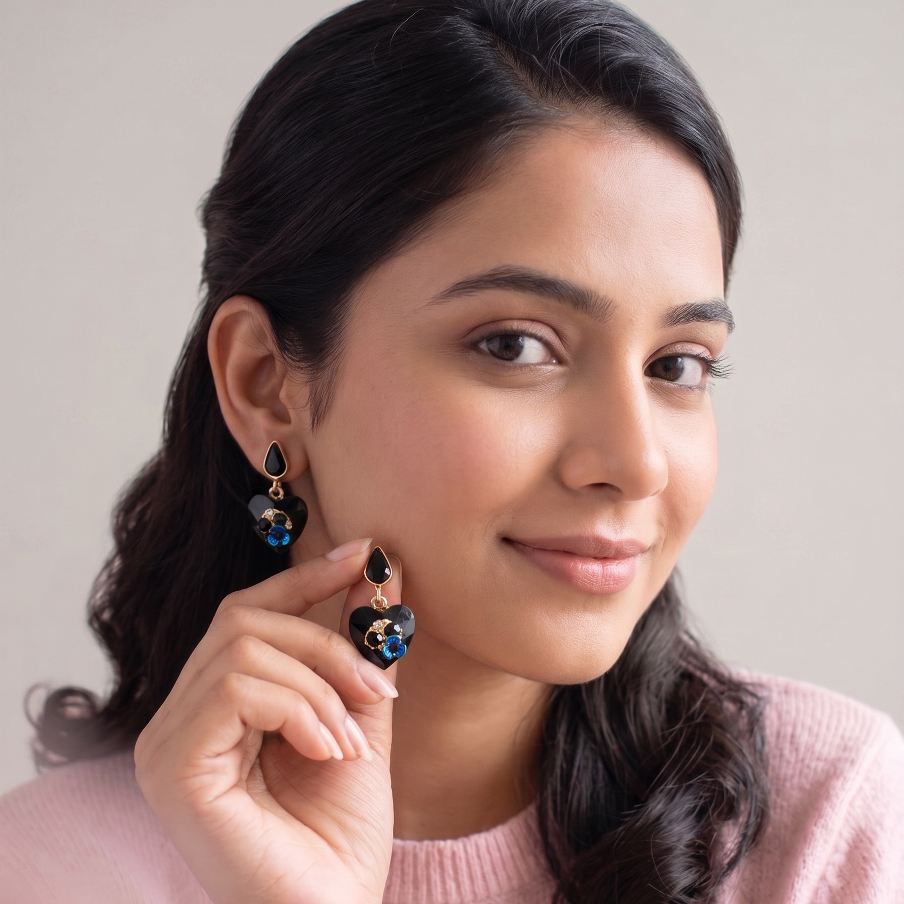 Woman wearing black heart-shaped earrings with blue stones, holding one earring to show it.