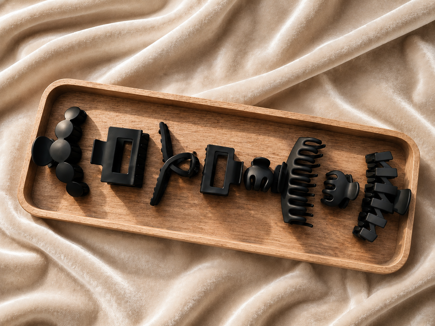 Set of black hair styling tools on a wooden tray with beige fabric background