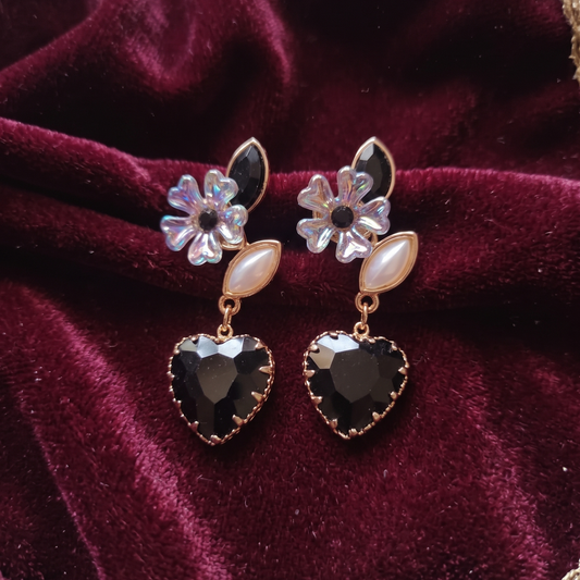 Pair of earrings with floral and heart designs on a burgundy velvet background