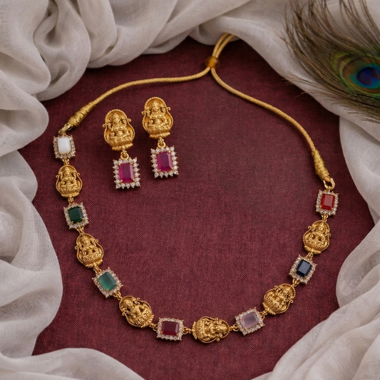 Gold necklace with colorful gemstones and matching earrings on a maroon fabric background.