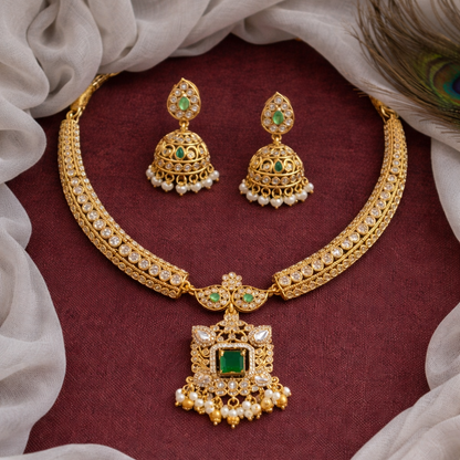 Gold necklace and earrings with green gemstones on a maroon fabric background