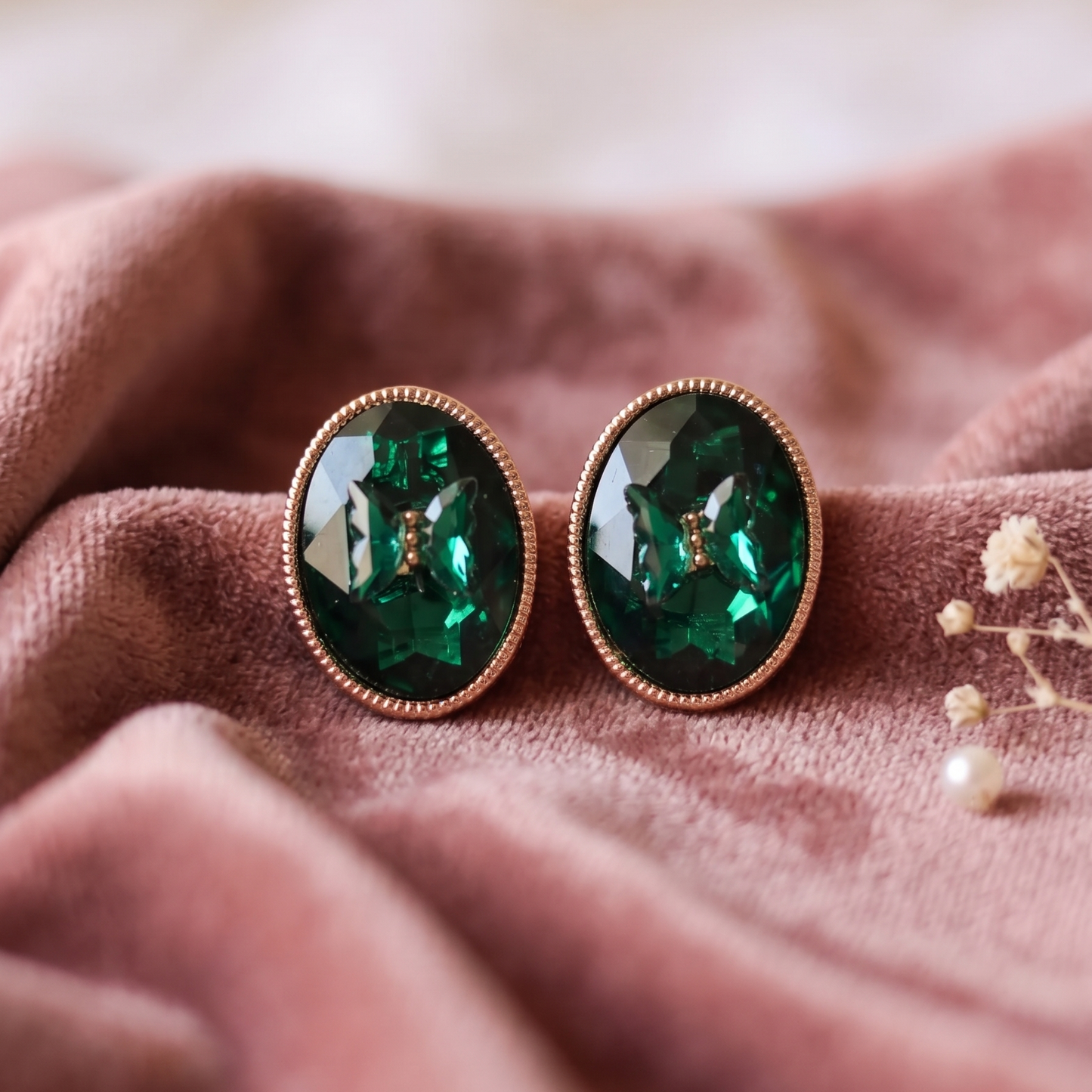 Pair of green gemstone earrings on a pink fabric background