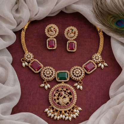Gold necklace and earrings with red and green gemstones on a maroon fabric background.