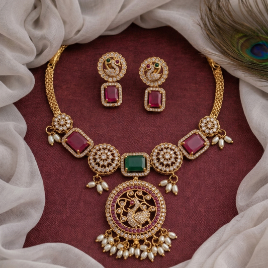 Gold necklace and earrings with red and green gemstones on a maroon fabric background.