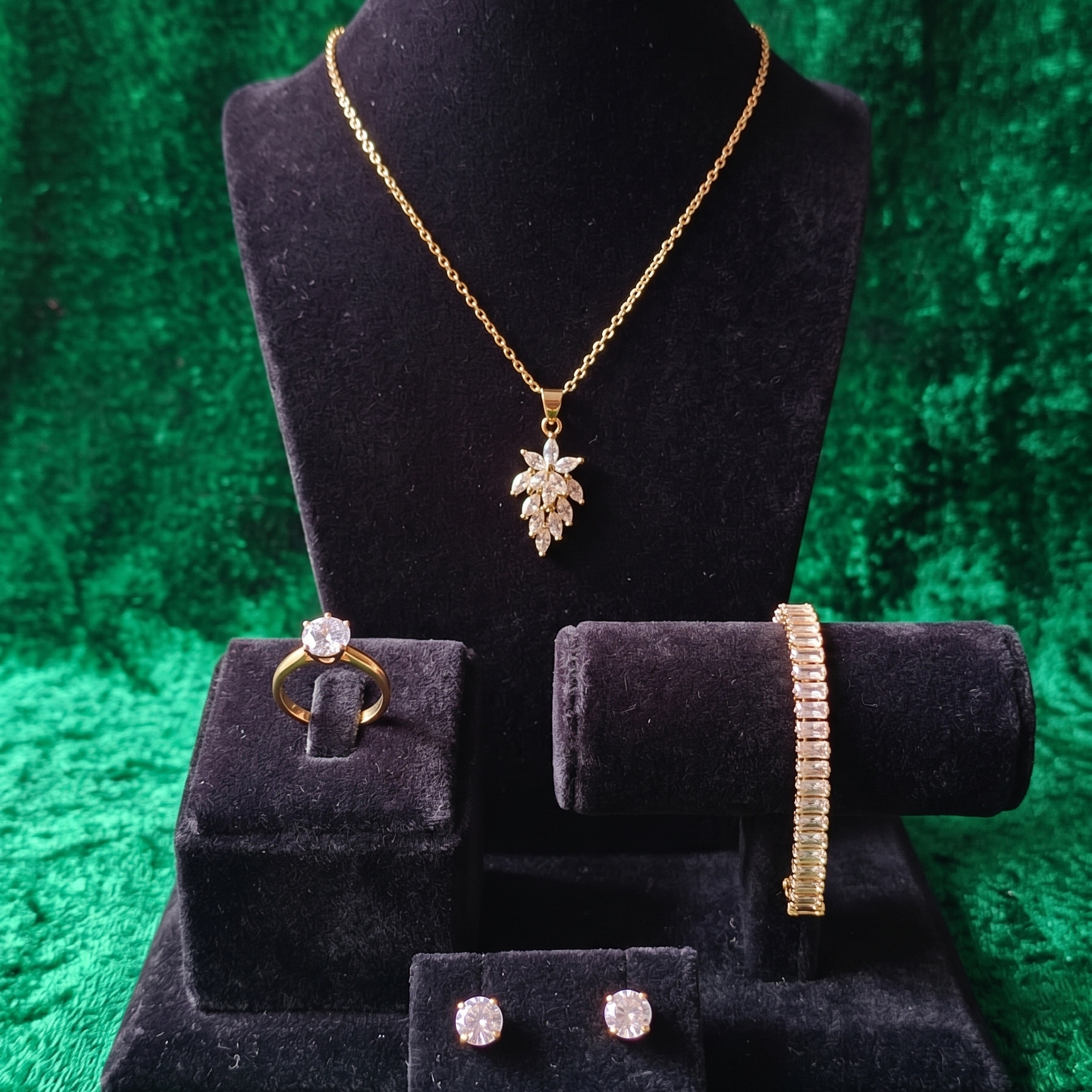 Jewelry set including necklace, ring, bracelet, and earrings on a black velvet stand against a green textured background.