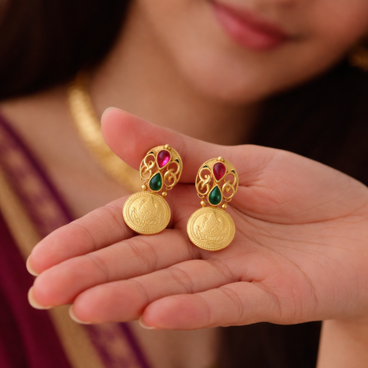 Gold earrings with gemstones held in a hand, blurred background