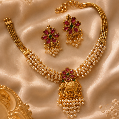 Gold jewelry set with pearls and gemstones on a textured beige surface