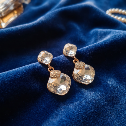 Gold earrings with clear gemstones on a blue velvet surface